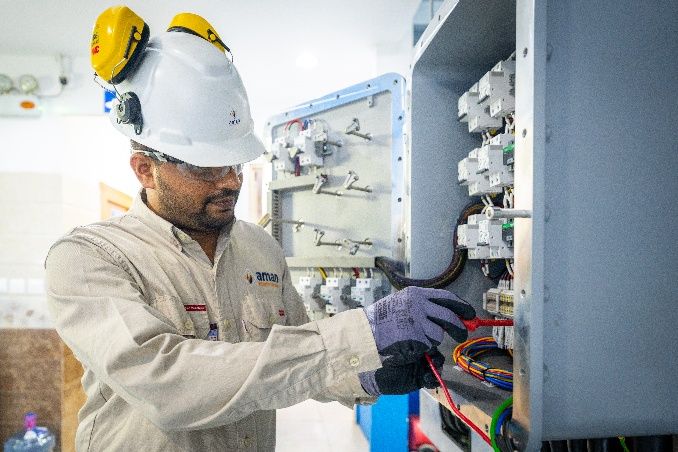 AIC technician in hard hat and ear defenders wiring an analyzer panel